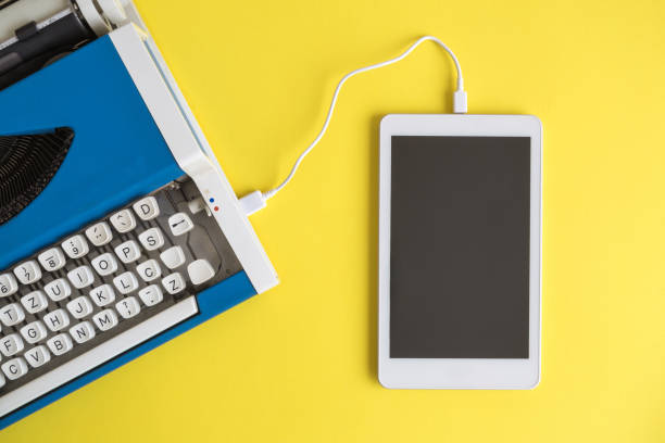 High angle view of vintage typewriter connected with digital tablet on yellow.