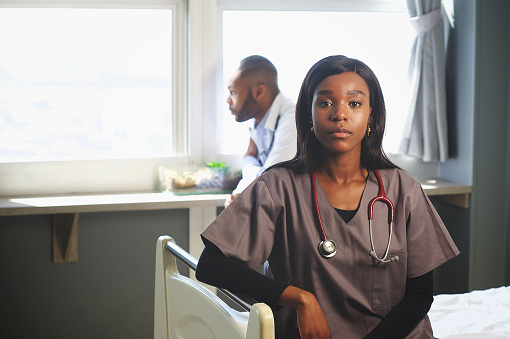 Portrait of a beautiful professional young African-American doctor sitting on bed with male doctor behind staring out of the window Cape Town South Africa