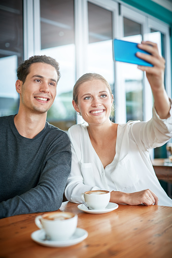 Attractive young couple sit in a coffee shop take a smiling selfie.