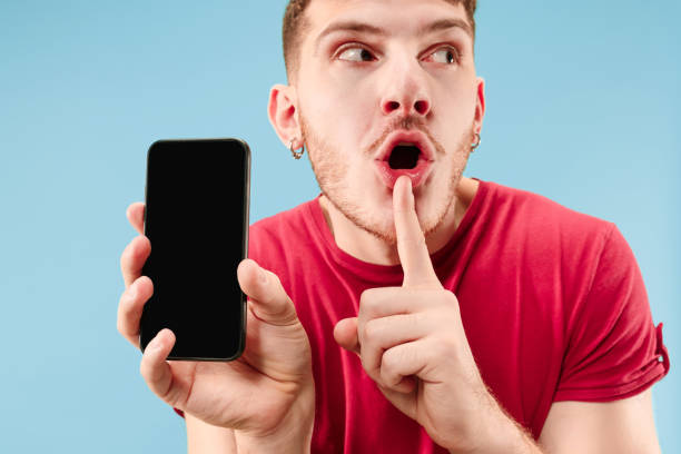 istock Young handsome man showing smartphone screen isolated on blue background in shock with a surprise face 1126069177