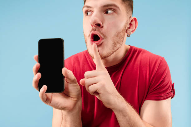 istock Young handsome man showing smartphone screen isolated on blue background in shock with a surprise face 1126069178