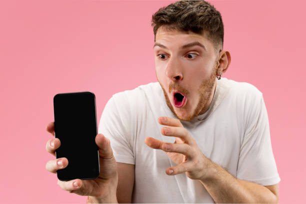 istock Young handsome man showing smartphone screen isolated on pink background in shock with a surprise face 1126069208