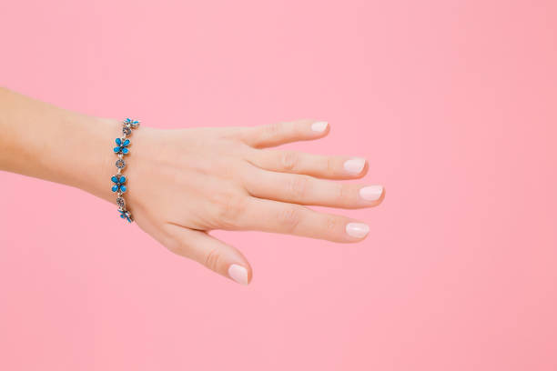 Blue flower bracelet on woman's wrist. Isolated on pastel pink background. Care about hand skin and nails. Closeup. Blue flower bracelet on woman's wrist. Isolated on pastel pink background. Care about hand skin and nails. Closeup. bijou personal accessory stock pictures, royalty-free photos & images