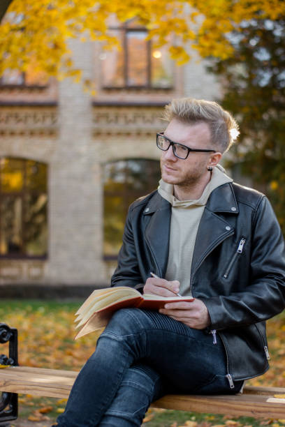 istock Writer in casual clothes makes notes in a notebook and sits on a park bench 1126070450