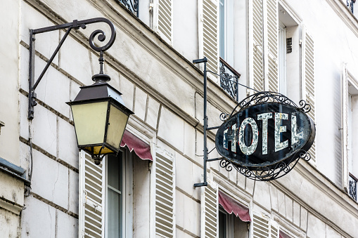 The period sign of a modest hotel, made of wrought iron and glass, on the facade of an old building with a vintage street light in a touristic district of Paris.