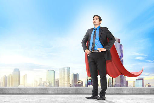 Attractive asian businessman with superhero cape standing on the rooftop of building in the city