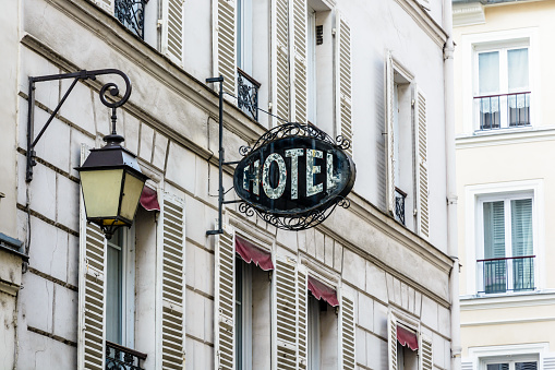 The period sign of a modest hotel, made of wrought iron and glass, on the facade of an old building with a vintage street light in a touristic district of Paris.