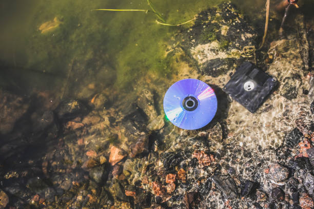 disco cd y disquete yacen en el lago al aire libre. olvidado más allá de concepto en el agua. - river stones audio fotografías e imágenes de stock