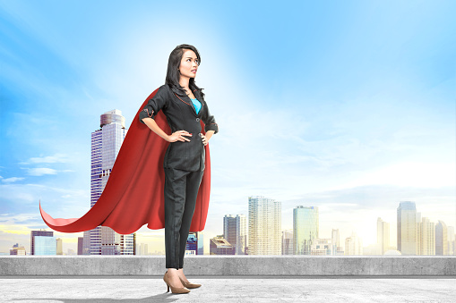Young asian business woman with red cape standing on the rooftop with cityscapes background