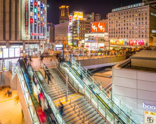 Crowds of shoppers and commuters on the elevated walkways outside Osaka Station, overlooked by the neon billboards and crowded highrises of Japan's vibrant second city.