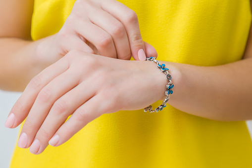 Woman in yellow, bright clothes wearing blue flower bracelet on her hand wrist. Daily beauty. Front view. Closeup.
