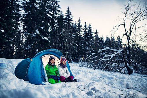 Kids having fun playing camping in winter forest. Brother and sister sitting in tent enjoying looking at winter view.\nNikon D850