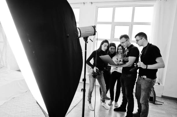 istock Photographer explaining about the shot to his team in the studio and looking on laptop. Talking to his assistants holding a camera during a photo shoot. Teamwork and brainstorm. 1126076009