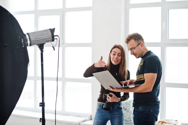 istock Photographer explaining about the shot to his assistant in the studio and looking on laptop. Teamwork and brainstorm. 1126076090