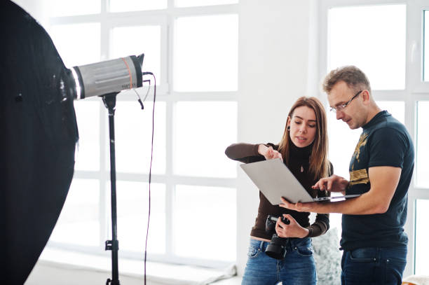 istock Photographer explaining about the shot to his assistant in the studio and looking on laptop. Teamwork and brainstorm. 1126076102