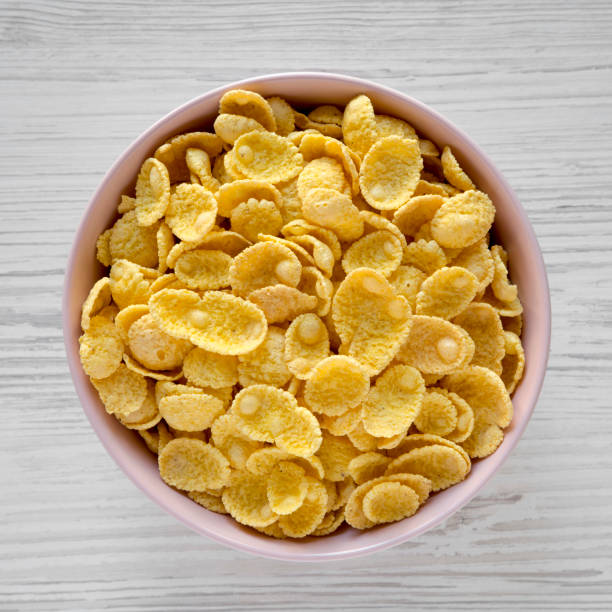 istock Corn flakes in a pink bowl for breakfast on a white wooden surface, overhead view. Flat lay, from above. Closeup. 1126076454