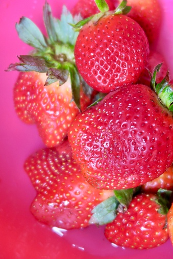 Fresh red strawberries, strawberry fruit, with green stalks, against a pink background.