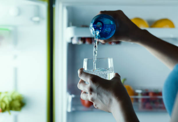 kobieta wyjmuje butelkę wody z lodówki i wlewa ją do szklanki - water water bottle glass pouring zdjęcia i obrazy z banku zdjęć