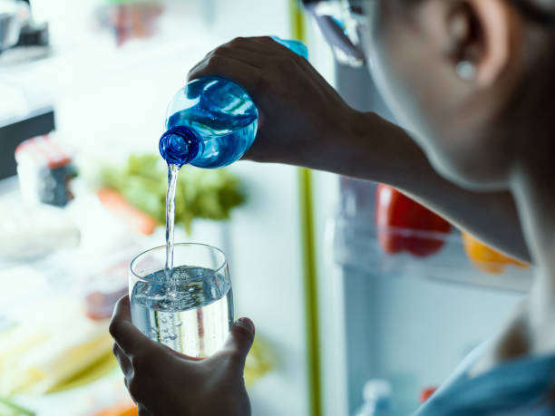 kobieta wyjmuje butelkę wody z lodówki i wlewa ją do szklanki - water water bottle glass pouring zdjęcia i obrazy z banku zdjęć