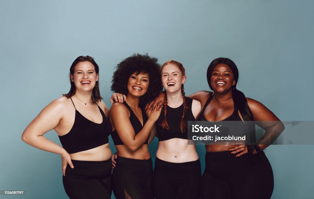 Diverse women embracing their natural bodies Portrait of group of women posing together in sportswear against a gray background. Multiracial females with different size standing together looking at camera and smiling. Women Stock Photo