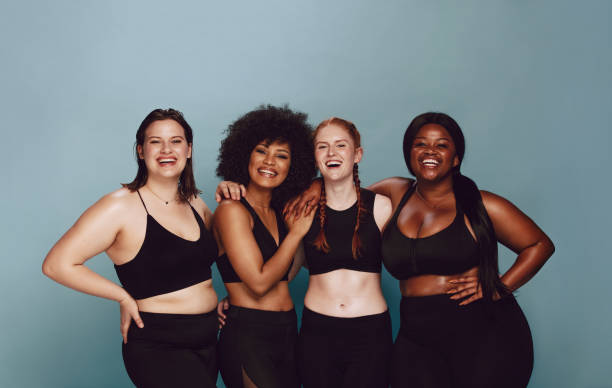 Diverse women embracing their natural bodies Portrait of group of women posing together in sportswear against a gray background. Multiracial females with different size standing together looking at camera and smiling. body positive stock pictures, royalty-free photos & images
