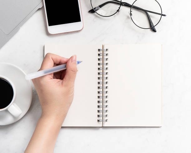 istock A woman is writing notes isolated on stylized marble office working desk with smartphone, laptop, glasses and coffee, mock up, topview, flatlay, copyspace, closeup 1126091482