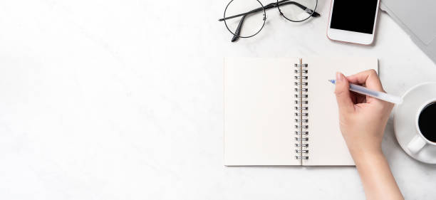 istock A woman is writing notes isolated on stylized marble office working desk with smartphone, laptop, glasses and coffee, mock up, topview, flatlay, copyspace, closeup 1126091489