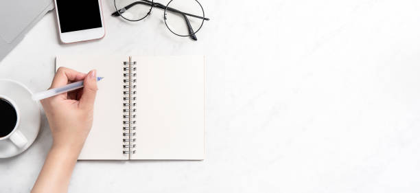 istock A woman is writing notes isolated on stylized marble office working desk with smartphone, laptop, glasses and coffee, mock up, topview, flatlay, copyspace, closeup 1126091538