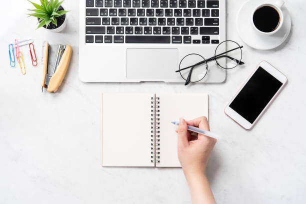 istock A woman is writing notes isolated on stylized marble office working desk with smartphone, laptop, glasses and coffee, mock up, topview, flatlay, copyspace, closeup 1126091546