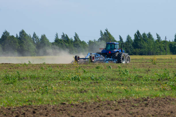istock Tractor plowing the green field with dust swirling 1126093327