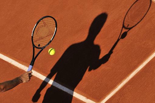 tennis ball laying on the court with a racket shadow