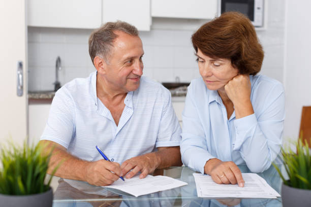 istock Smiling mature couple  at table in home kitchen filling up documents 1126103112