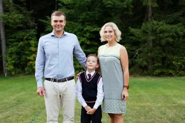 Vilnius, Lithuania - September 1, 2015: family of three in their formal clothes are smiling and posing for a photo on the first day at school.