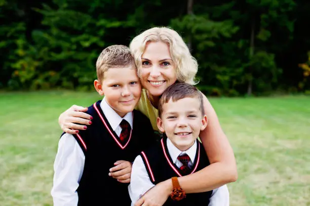 Vilnius, Lithuania - September 1, 2015: beautiful mother is hugging her two sons dressed in blue waistcoats and neckties and posing for a family portrait on the first day to school.