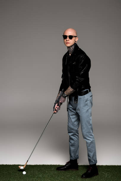 istock stylish tattooed man in sunglasses and leather jacket playing golf on grey 1126105577