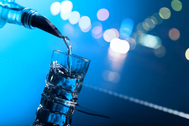 Vodka is poured from the bottle into a glass, reflective background, blue light.