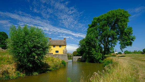 Bridgewater, United Kingdom - August 3, 2018:  A mid day view in summer of the best surviving example of a 10th Century Moat and Bailey Castle, Stogursey Castle, which is now a Landmark Trust property.  The castle was controlled by King John of England during the First Barons' War, and was ordered to be destroyed in 1215, but survived; John's lieutenant Falkes de Breauté took control of the castle, and after his death a second order to destroy the property was given in 1228, again apparently ignored. The castle was extended in stone in 1300 by the Fitzpayne family, but was destroyed in the 1450s by the Yorkist faction during the War of the Roses. A house was built within the castle grounds in the 17th century and was restored in the 1870s, but by the late 20th century had itself become ruined.  This picture was taken after the completion of recent refurbishment work.