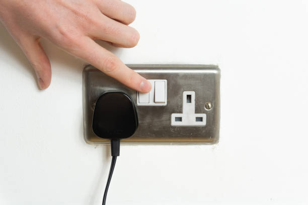 istock Stainless steel UK plug socket on white wall with hand switching on 1126110818