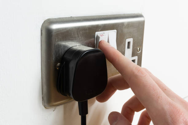 istock Stainless steel UK plug socket on white wall with hand switching on 1126111445
