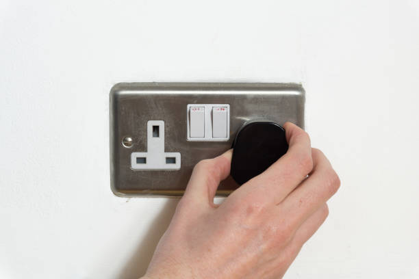 istock Stainless steel UK plug socket on white wall with hand plugging something in 1126112269