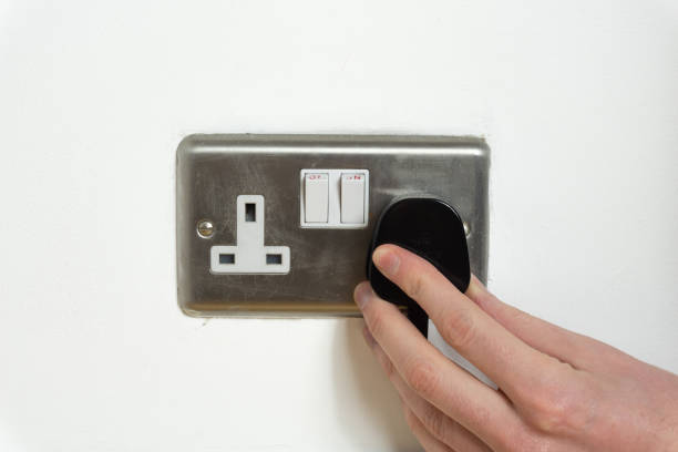 istock Stainless steel UK plug socket on white wall with hand plugging something in 1126112291