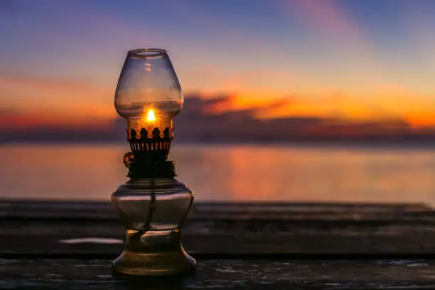 Photo of Beautiful old rustic oriental oil lamp silhouette in a beautiful amazing red velvet sunset sky at tropical island in Indian Ocean, Koh Phangan, popular tourist destination in Thailand.