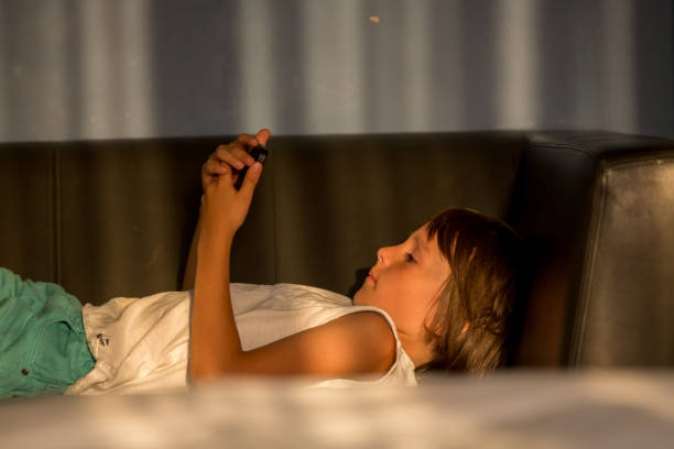 istock Preschool boy, lying down on sofa, playing on tablet on sunset 1126118022