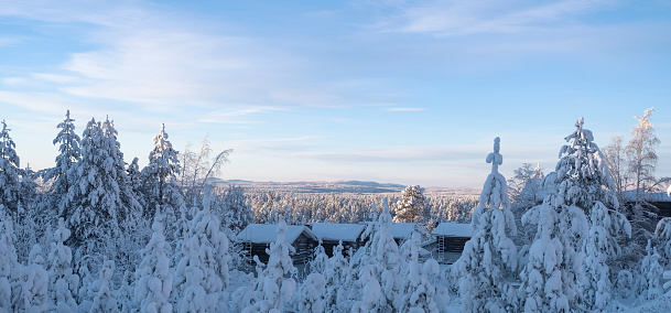 Winter landscape. Snow-covered forest and mountain on the horizon. Lapland Finland. Blue sky and some clouds. Wooden houses in the foreground.