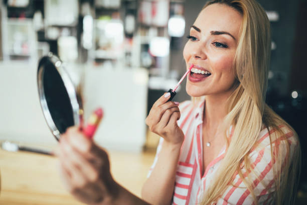 istock Beautiful young woman applying lips makeup at home 1126123316