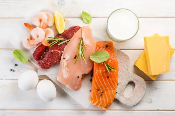 Selection of aminal protein sources - beef, chicken, salmon, cheese, milk, eggs, shrimps on wood background