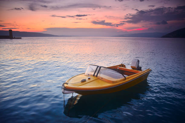 Small, old school and vintage, yellow-orange speed boat in the port, during the summer sunset. Lonesome concept, ideal for large prints, significant amount of noise may appear. small boat stock pictures, royalty-free photos & images