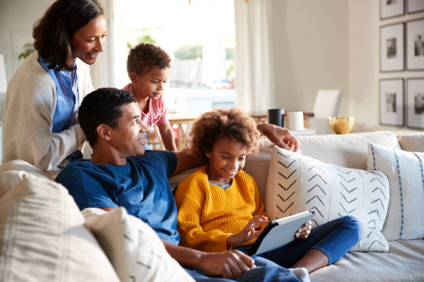 istock Father and daughter sitting on sofa using tablet computer, mother and toddler son leaning behind them, low angle 1126137806