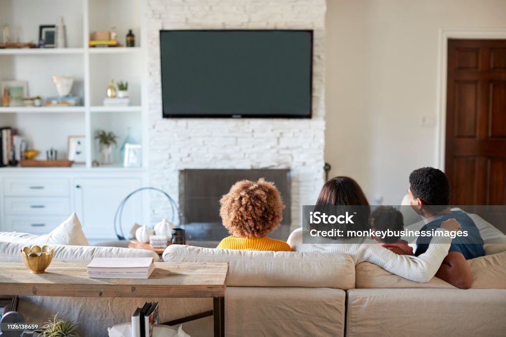 Vue arrière du jeune famille assise sur le canapé et regardent la télévision ensemble dans leur salon - Photo de Famille libre de droits
