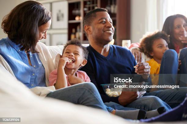 Three Generation Family Family Sitting On The Sofa In Living Room Watching Tv And Eating Popcorn Selective Focus Stock Photo - Download Image Now